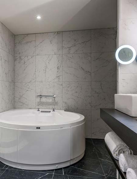 Salle de bain de l’Hôtel du Roi à Carcassonne avec baignoire ronde et revêtement céramique effet marbre