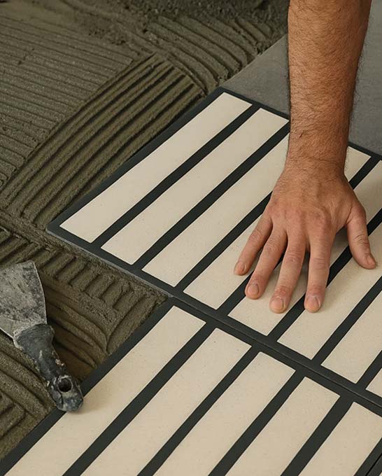 Pose artisanale de carreaux de ciment décoratifs sur lit de mortier pour garantir l’adhérence et la durabilité du revêtement