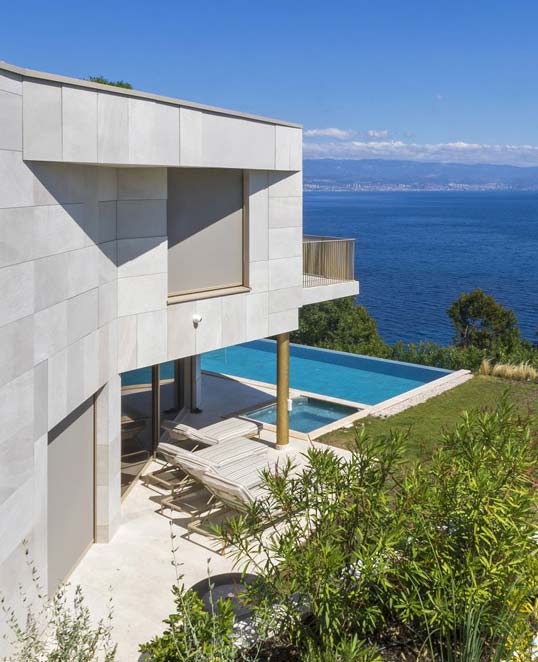 Carrelage de façade effet pierre pour intégration architecturale naturelle Façade contemporaine habillée de carrelage effet pierre claire intégrée au paysage côtier avec terrasse et piscine